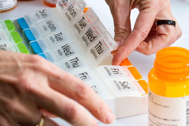 Ruka otvara nedeljni organizator za lekove sa označenim danima i dozama uz bočicu tableta.