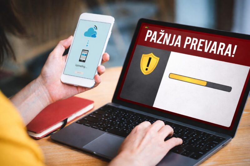 Osoba koristi telefon i laptop dok se na ekranu prikazuje upozorenje na potencijalnu online prevaru