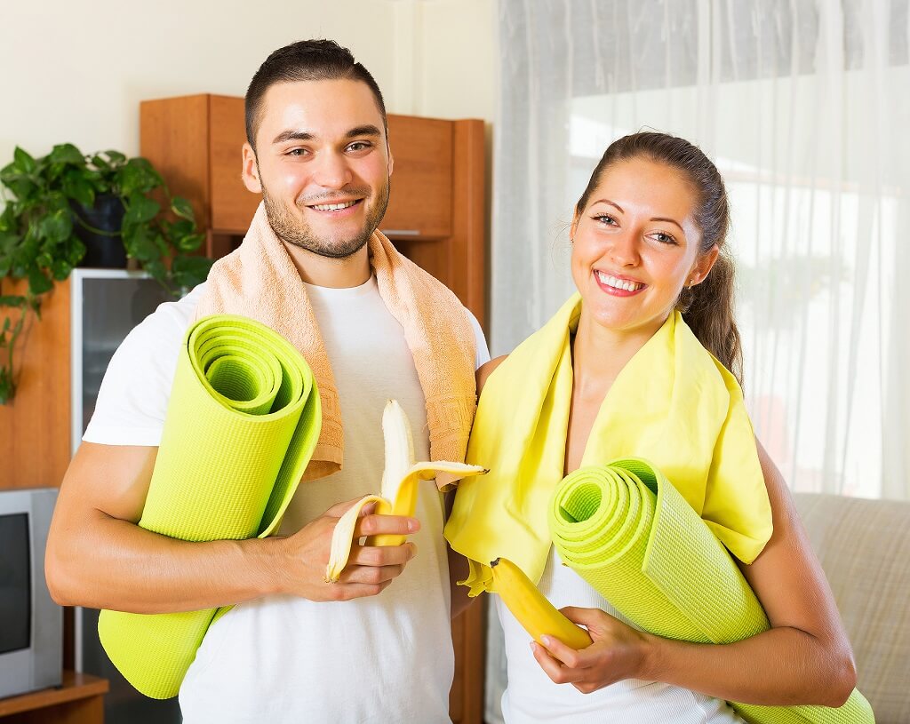 Momak i devojka drže banane i prostirke za vežbanje