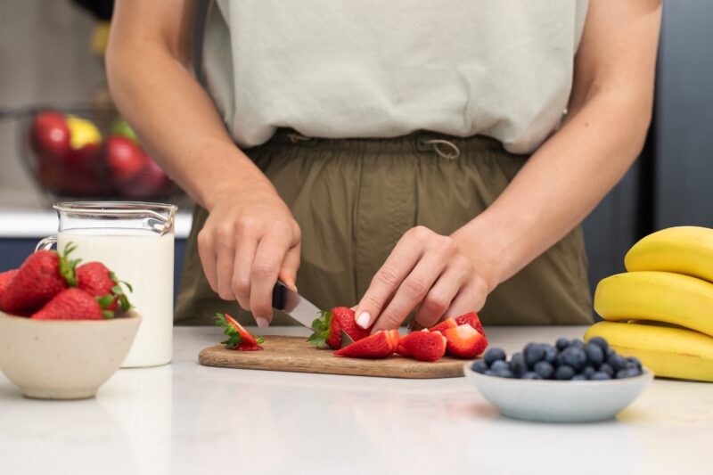 devojka seče kagode na dasci pored banane, borovnice i jogurt