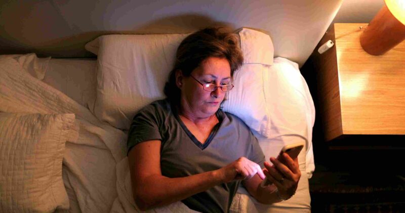Osoba leži u krevetu i koristi telefon noću