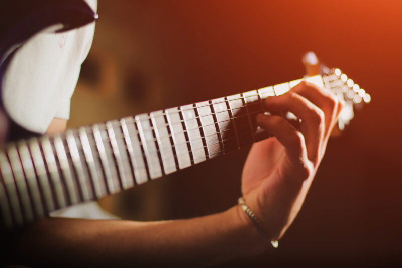 Ruka svirača na vratu električne gitare uz toplo osvetljenje