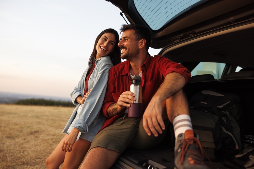 Par uživa u zajedničkom trenutku tokom vikend putovanja pored automobila u prirodi