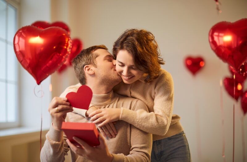 Par razmenjuje romantičan poklon za godišnjicu u prostoru ukrašenom crvenim srcima