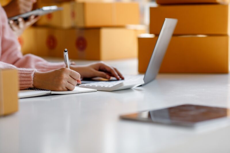 prikaz laptopa i osobe koja kucka nešto po jemu i zapisuje na papir