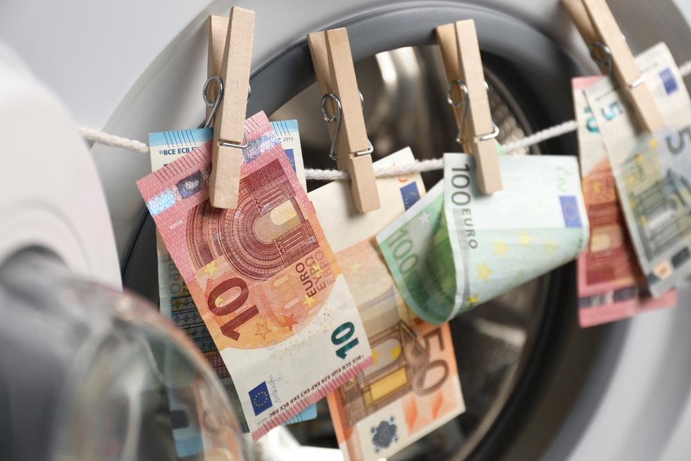 Novčanice evra okačene na štrik ispred mašine za pranje kao simbol provere porekla novca i AML kontrole